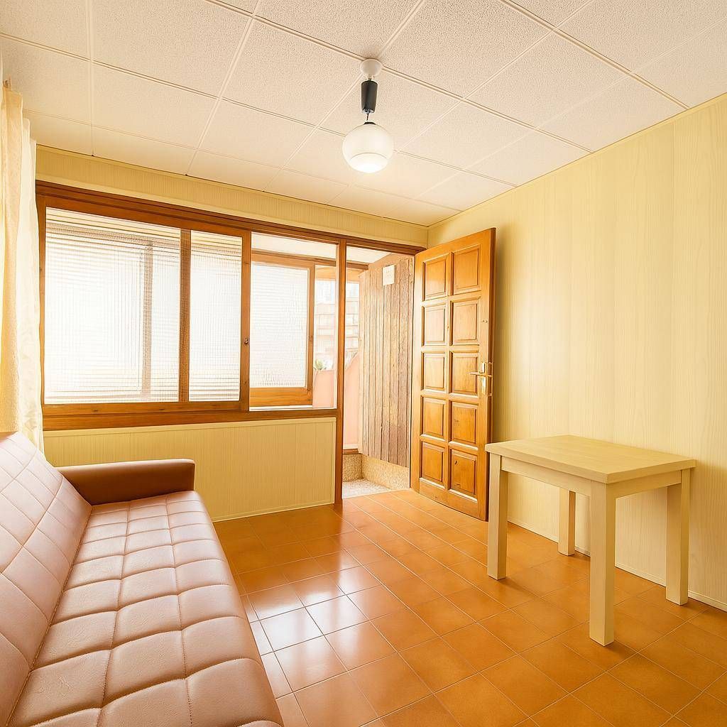 Sala de estar con suelo naranja, sofá marrón, puerta y ventana de madera y mesa blanca.
