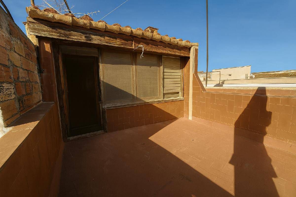 Azotea con un pequeño edificio deteriorado, con puerta y ventana. Pintura marrón anaranjada y luz solar.