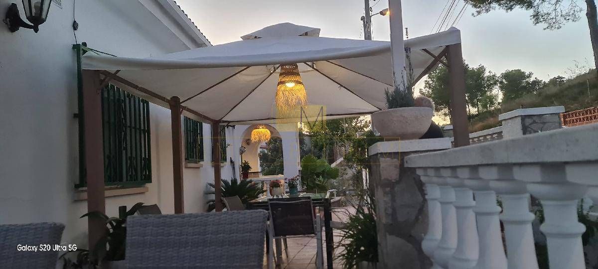 Zona de estar al aire libre cubierta con dosel blanco y luces, con vista a una barandilla de piedra y plantas.