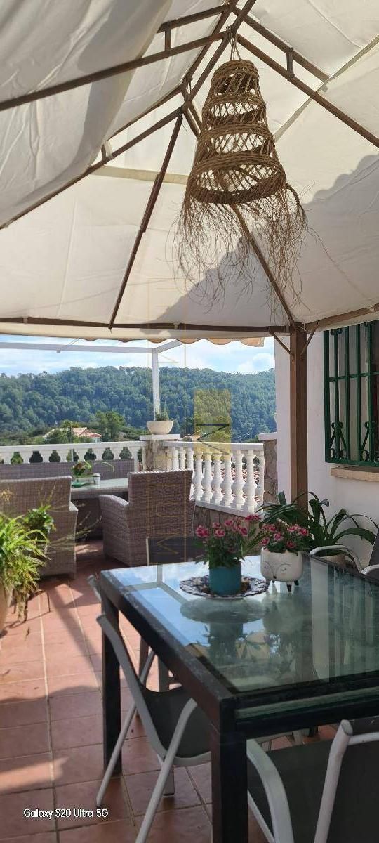 Patio exterior con mesa, sillas, plantas y vista a árboles y montañas.