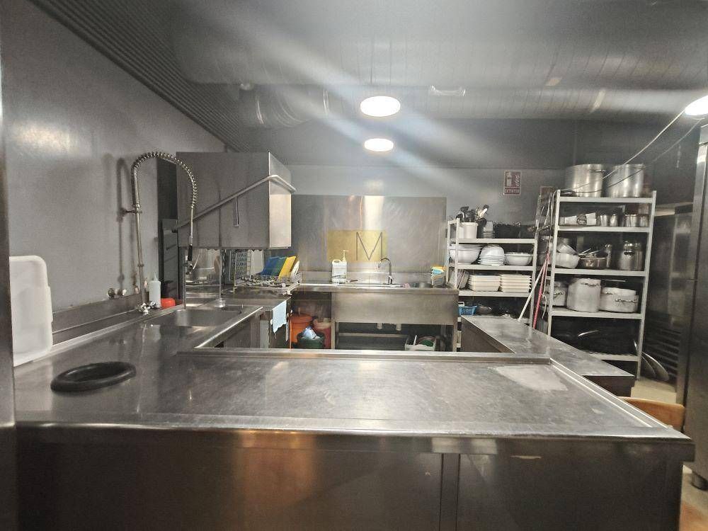 Cocina comercial de acero inoxidable con encimeras, fregaderos y estantes.