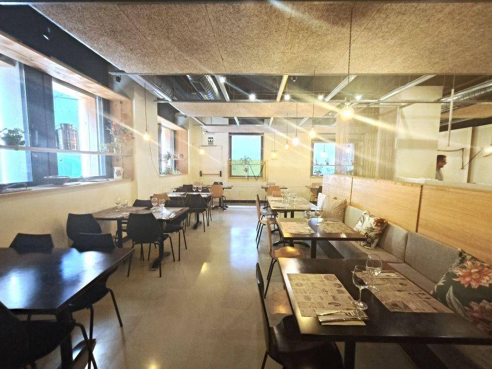 Interior de una cafetería con mesas y sillas. La luz natural entra a raudales por las ventanas.
