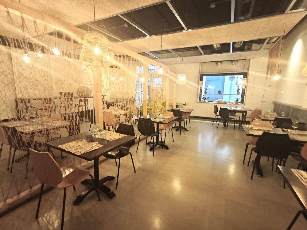 Interior de restaurante con mesas y sillas, cuerda decorativa y lámparas colgantes. Suelo gris y ventana al fondo.