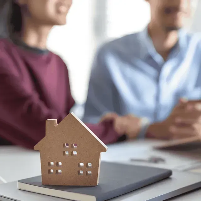 Casa en miniatura en un cuaderno con una pareja borrosa en el fondo