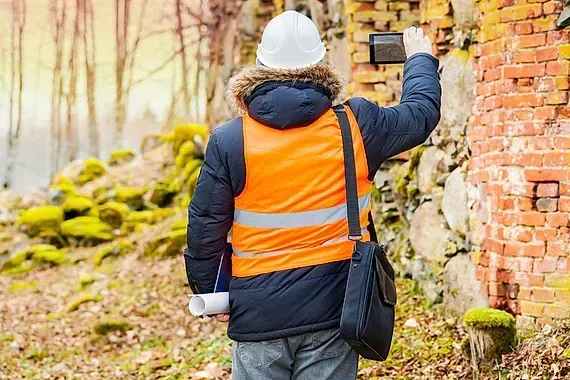 Un hombre que lleva un chaleco naranja y un casco está parado frente a una pared de ladrillos.