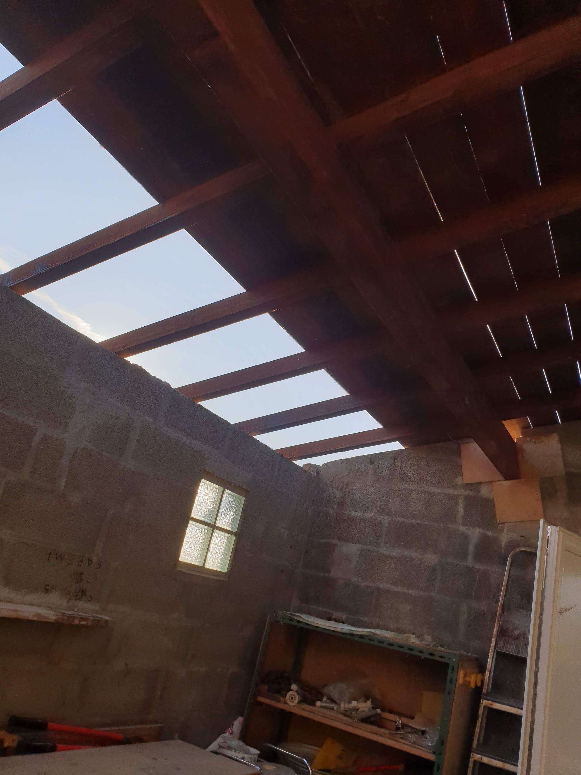 Vue intérieure d'une pièce avec un plafond à lattes de bois et des puits de lumière. Murs en parpaings et petite fenêtre.