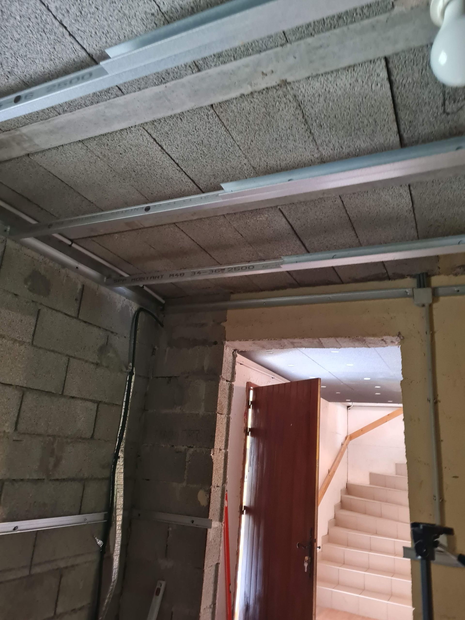 Intérieur d'un chantier de construction. Plafond et murs en parpaings gris, poutres de soutien métalliques, porte d'accès à l'escalier.