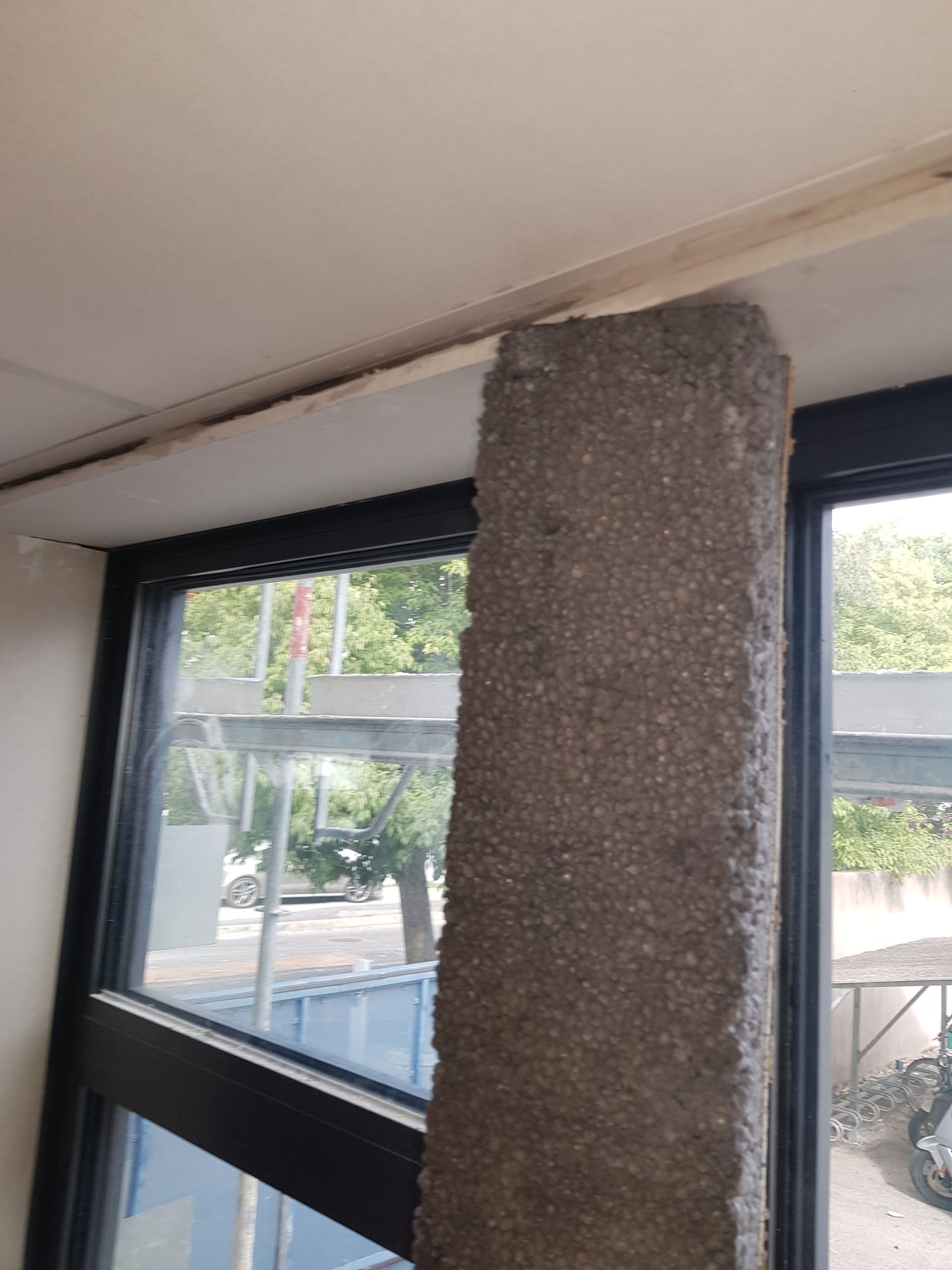 Pilier en béton gris à côté d'une fenêtre, soutenant un plafond.