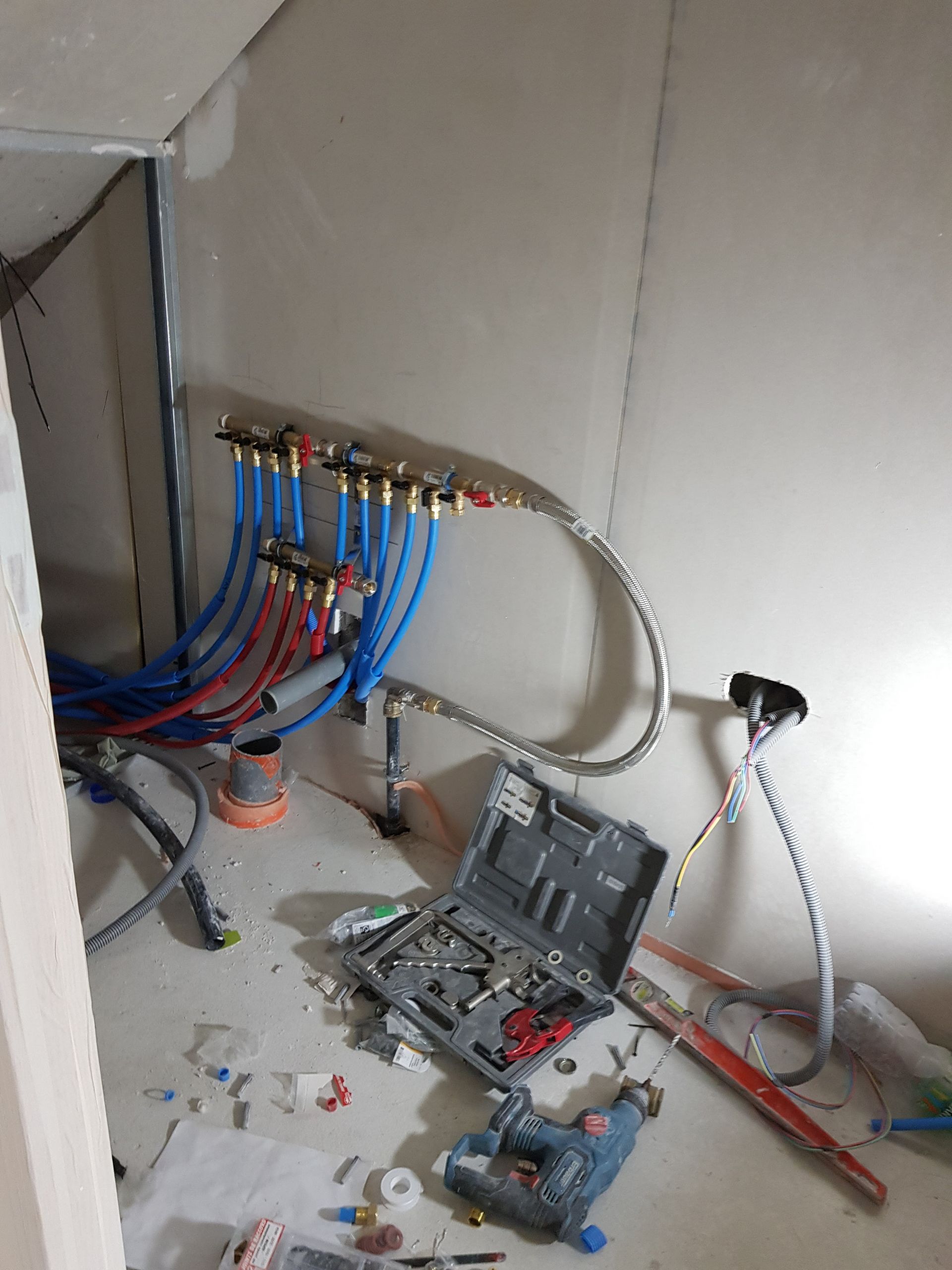 Installation de plomberie avec des tuyaux PEX bleus et rouges raccordés à un collecteur dans une pièce aux cloisons sèches non finies.