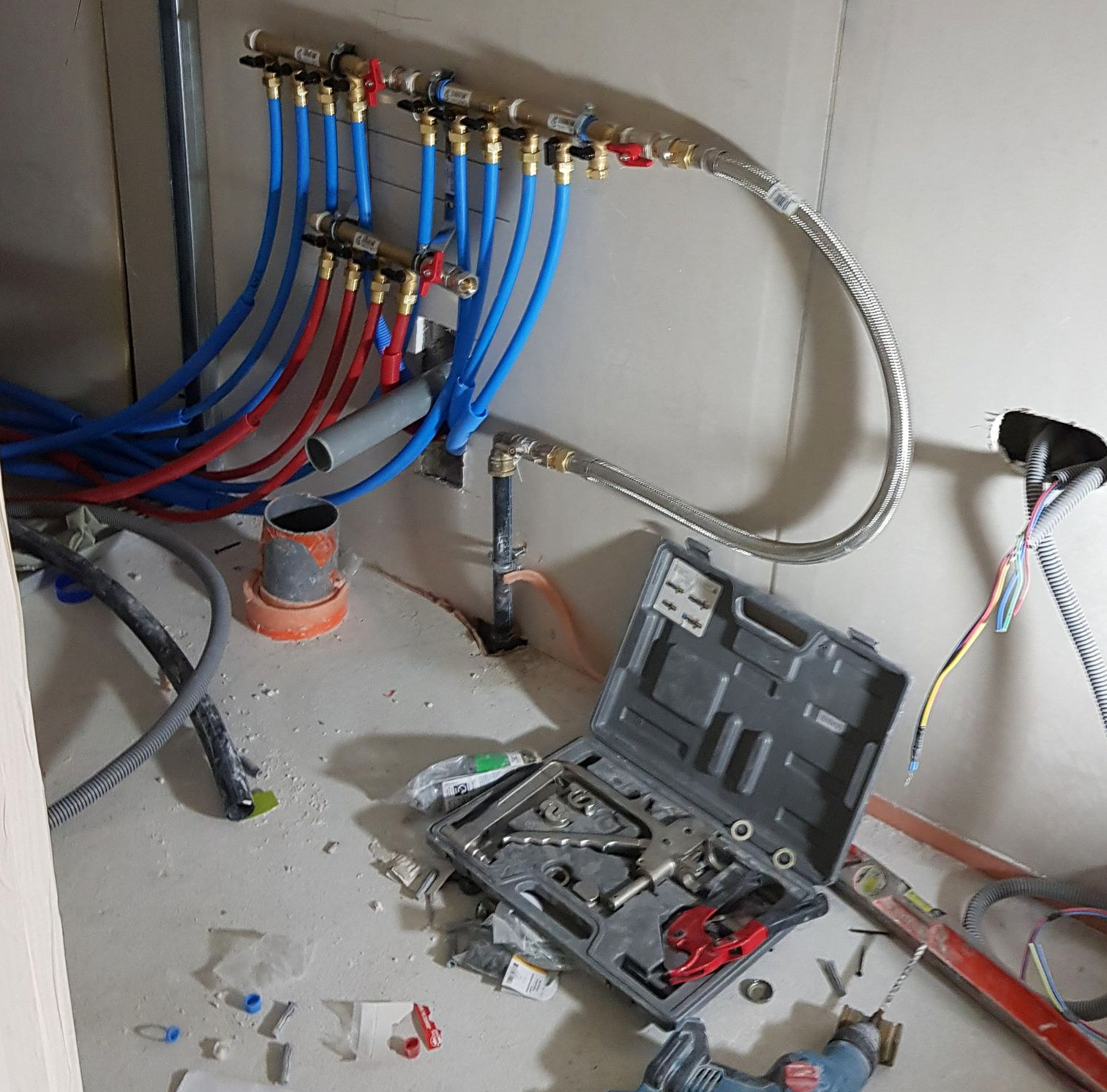 Tuyaux et outils de plomberie sur un chantier. Les tuyaux bleus et rouges sont raccordés à un collecteur de distribution.