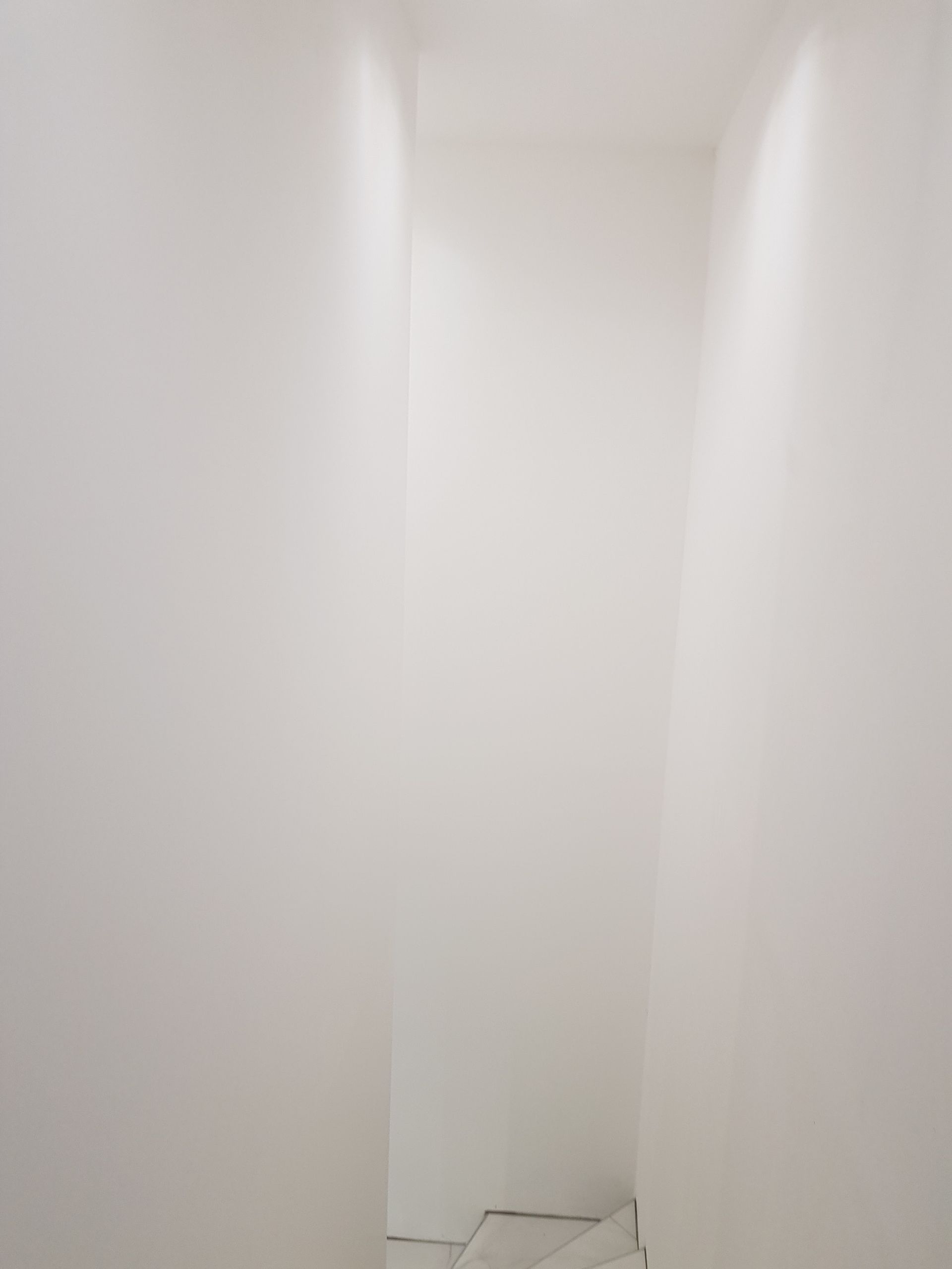 Couloir blanc avec éclairage zénithal, menant à une porte.