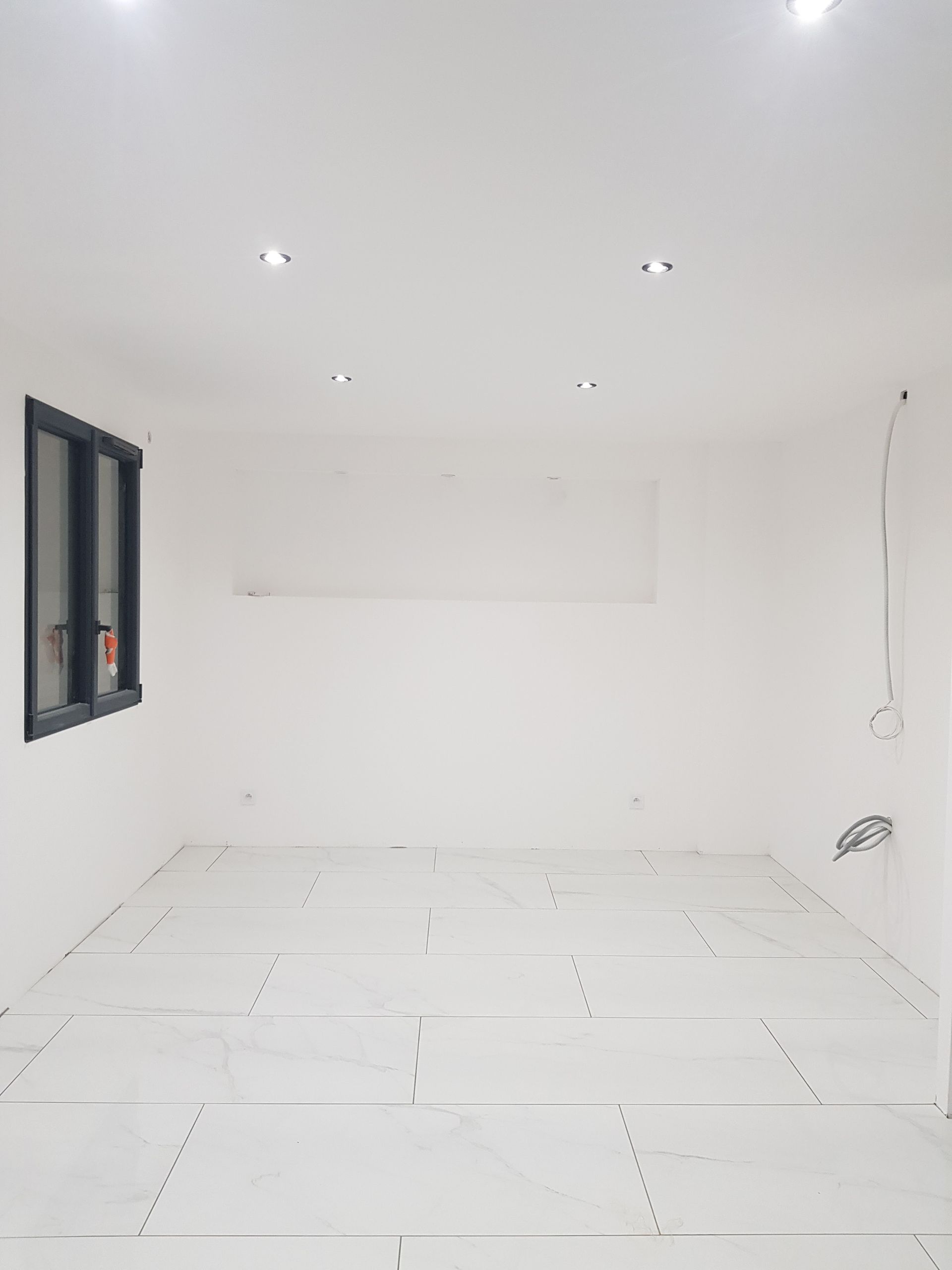 Pièce vide avec des murs blancs, du carrelage au sol et une fenêtre.