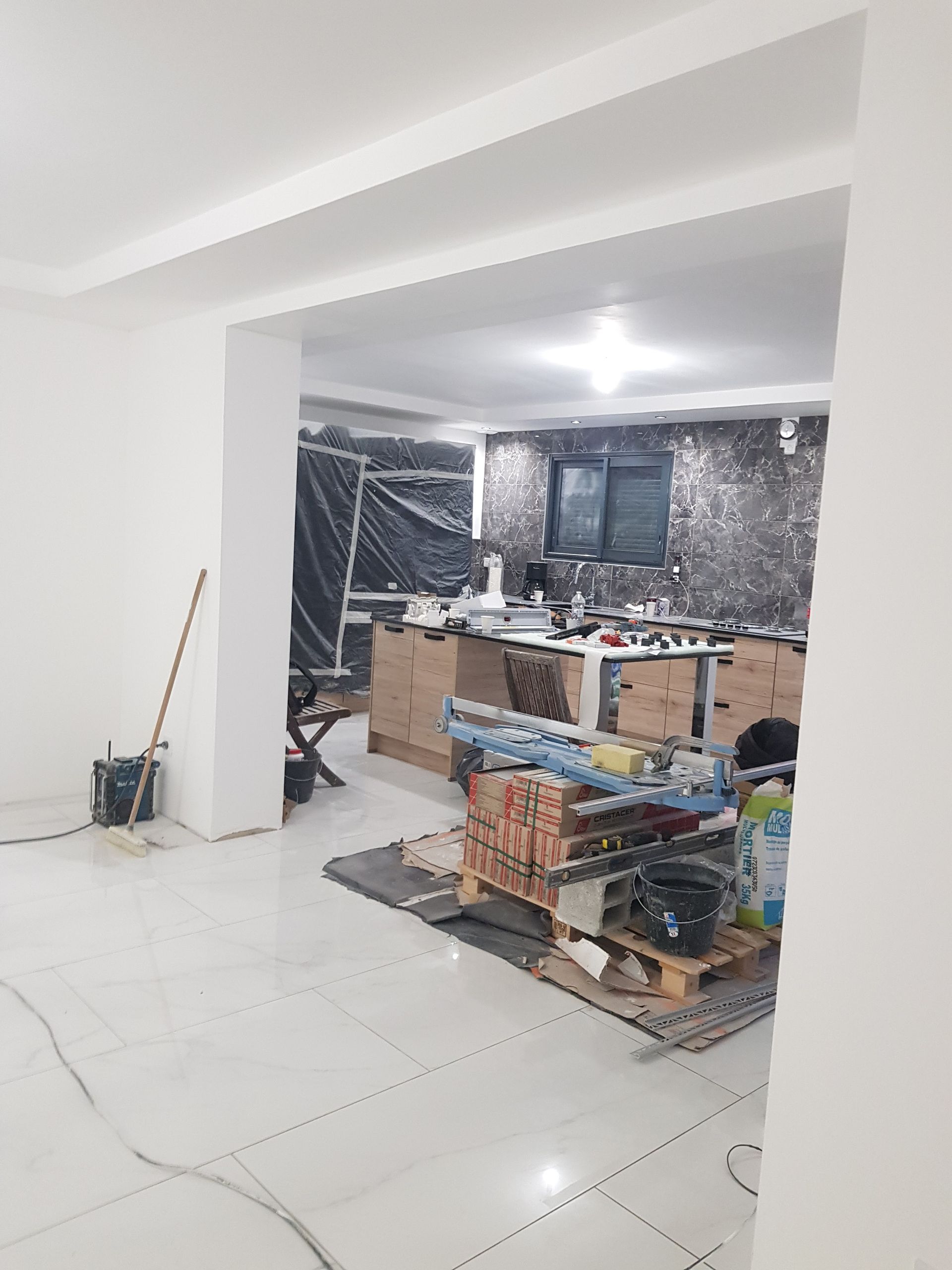 Vue intérieure d'une pièce en construction avec des murs blancs et un espace de travail avec des outils et des matériaux.