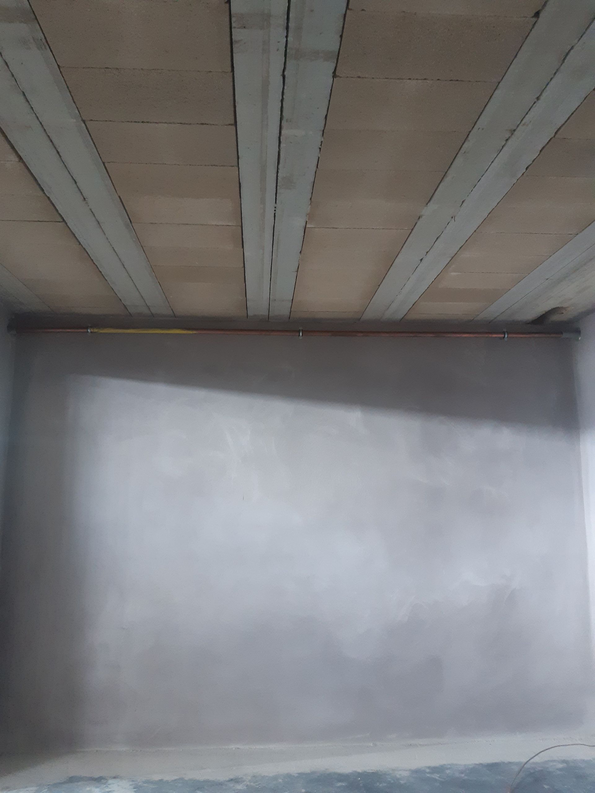 Pièce aux murs gris et au plafond texturé orné de poutres en béton. Le sol est également gris.