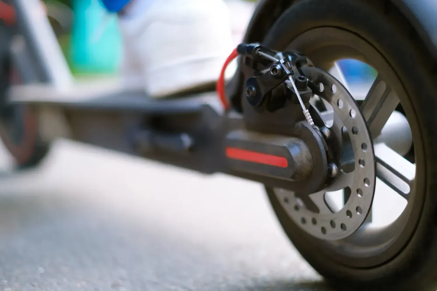 Vista de cerca del freno de disco trasero y la rueda de un patinete eléctrico gris.