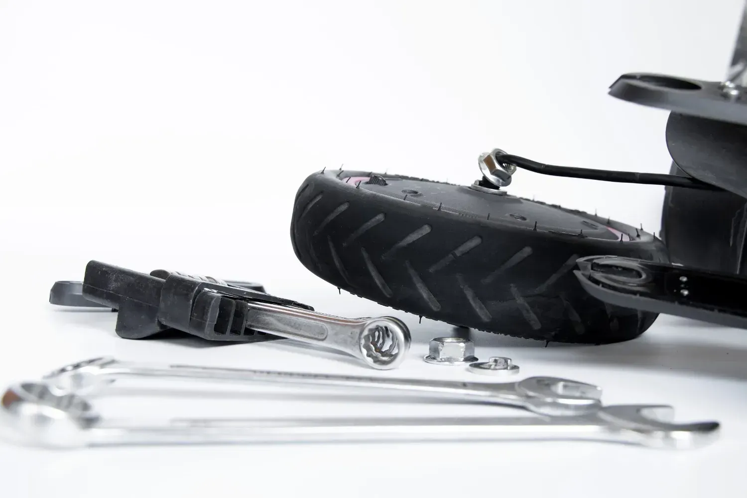 Primer plano de una rueda de patinete eléctrico desmontada y llaves inglesas metálicas sobre un fondo blanco.