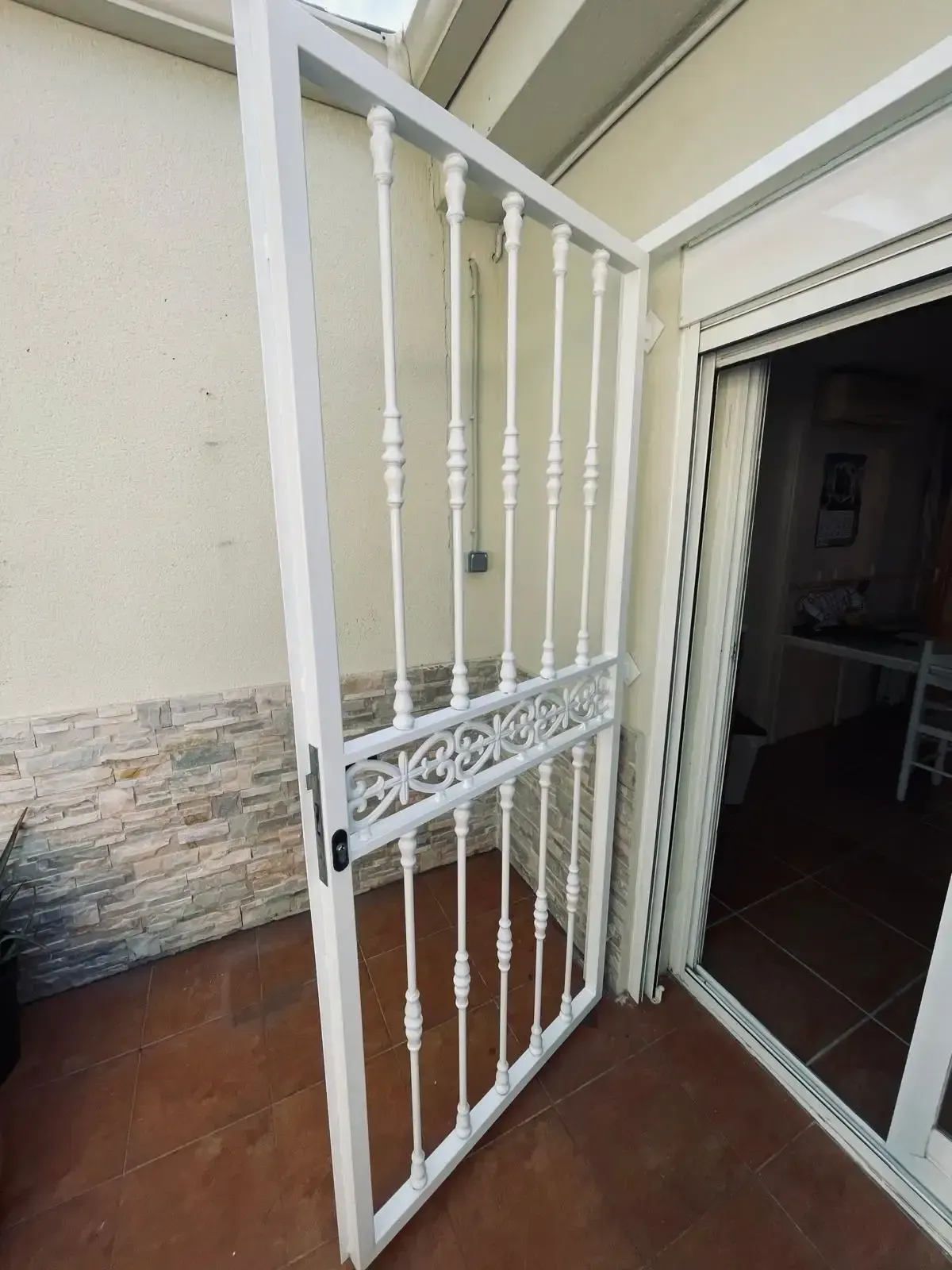 Puerta de seguridad metálica blanca abierta en la entrada de una casa, junto a una puerta con azulejos.