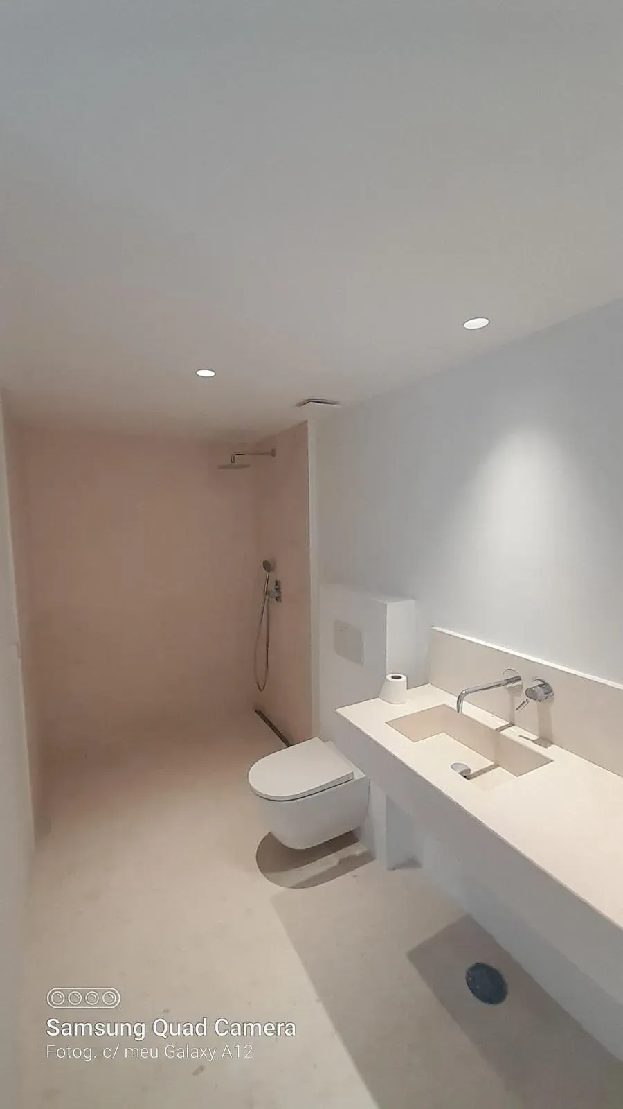 Baño moderno de color blanco con lavabo, inodoro, ducha y luces empotradas en el techo.