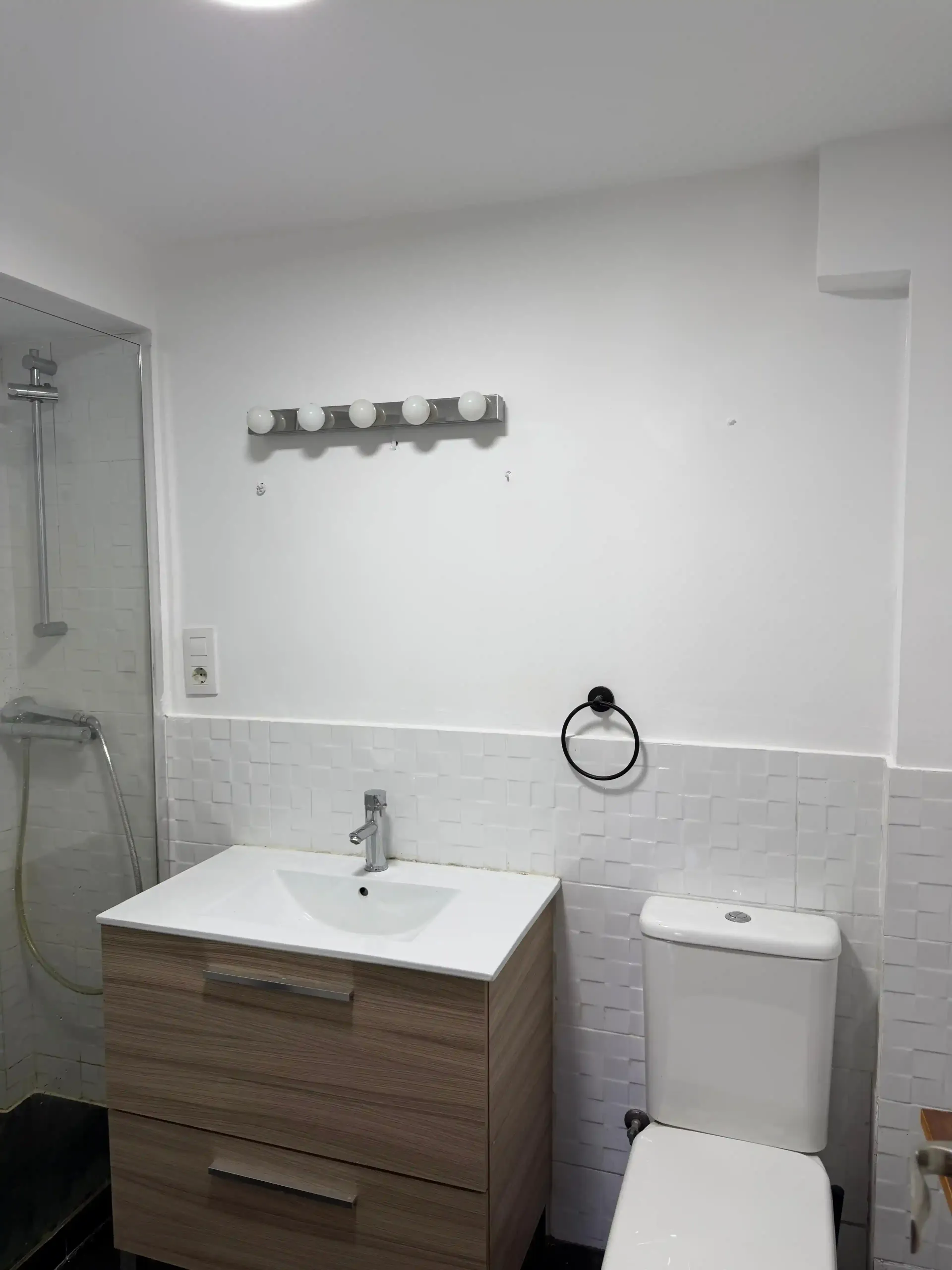 Baño pequeño de color blanco con lavabo, inodoro, ducha y ganchos para toallas.