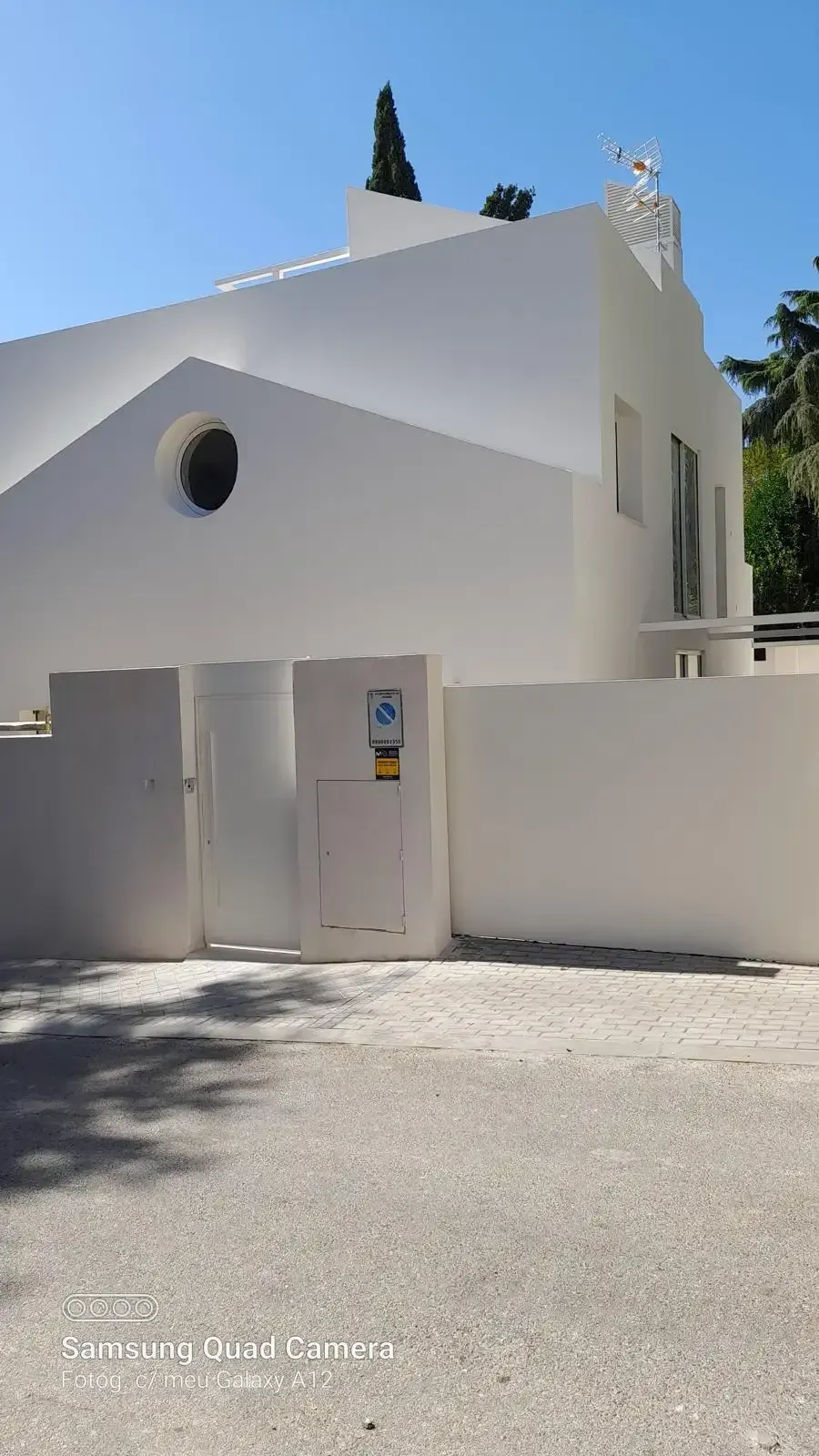 Casa moderna blanca con ventana redonda y entrada con verja bajo un cielo azul claro.
