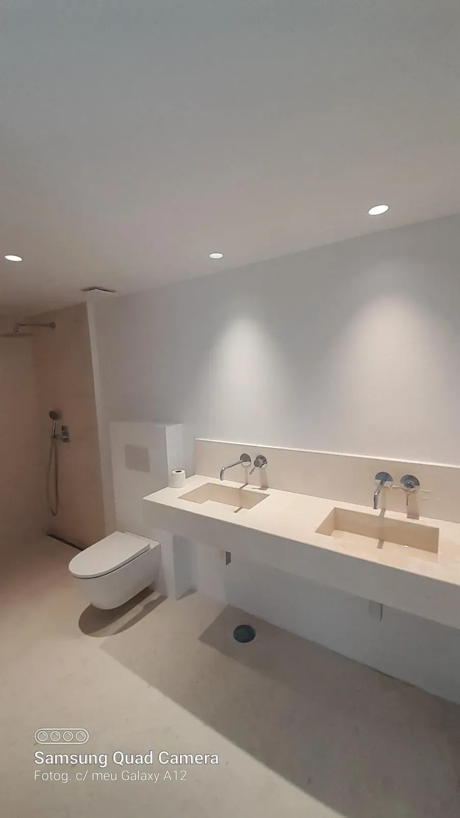 Baño moderno y accesible con lavabos dobles, inodoros suspendidos e iluminación tenue en el techo.