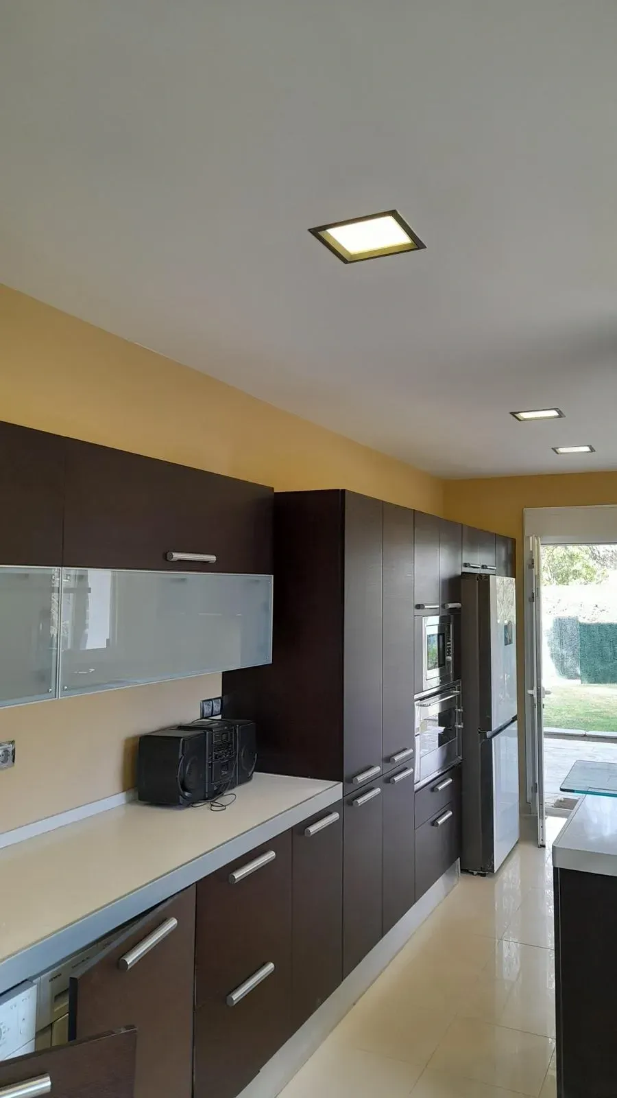 Cocina moderna con armarios oscuros, encimeras blancas y electrodomésticos integrados en un interior luminoso.