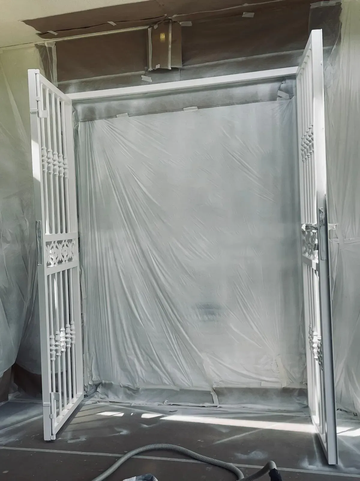 Puerta metálica blanca abierta frente a una puerta o ventana interior cubierta con plástico.