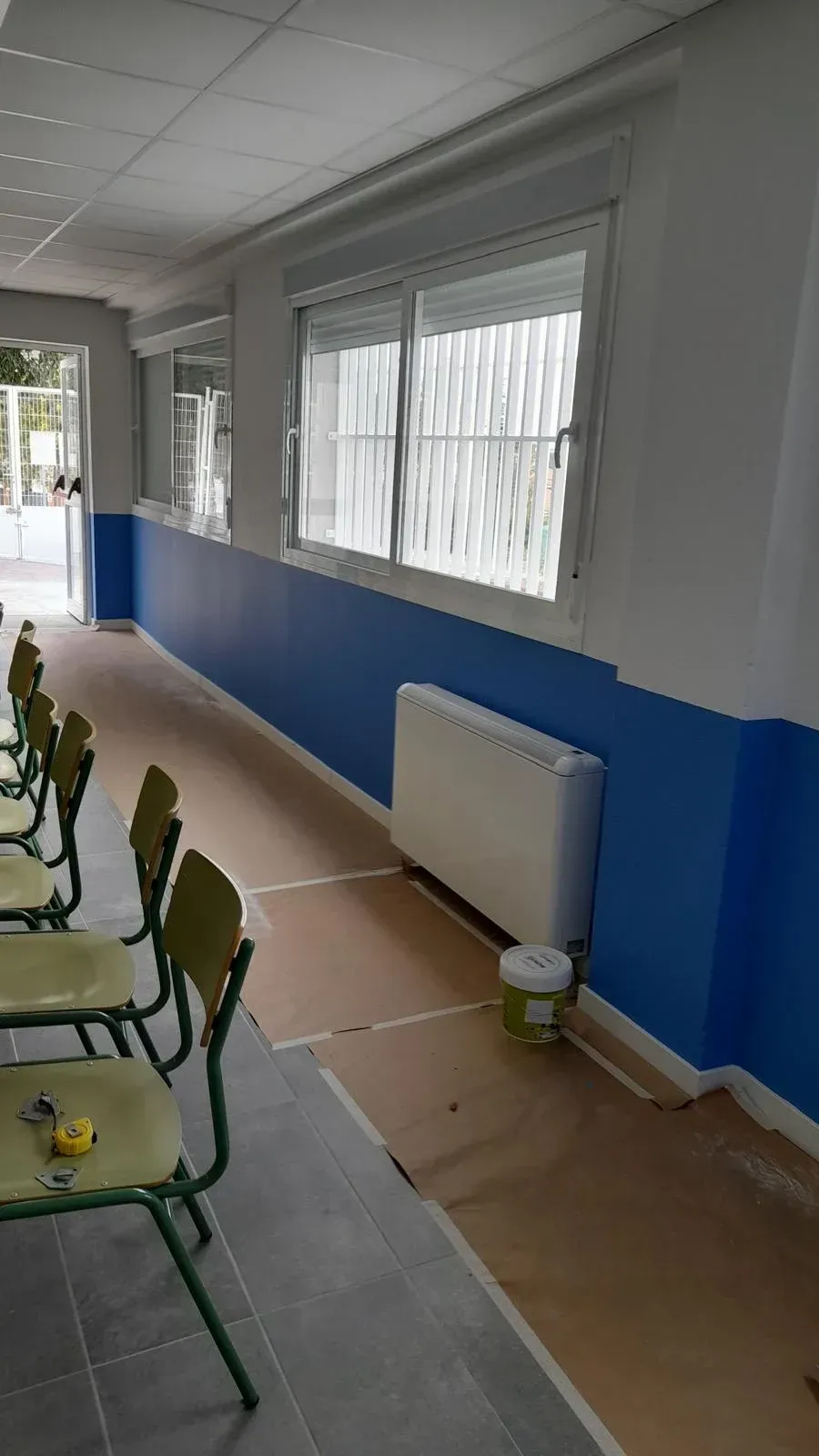Pasillo con paredes azules y blancas, ventanas, radiadores y sillas verdes a lo largo del lado izquierdo.