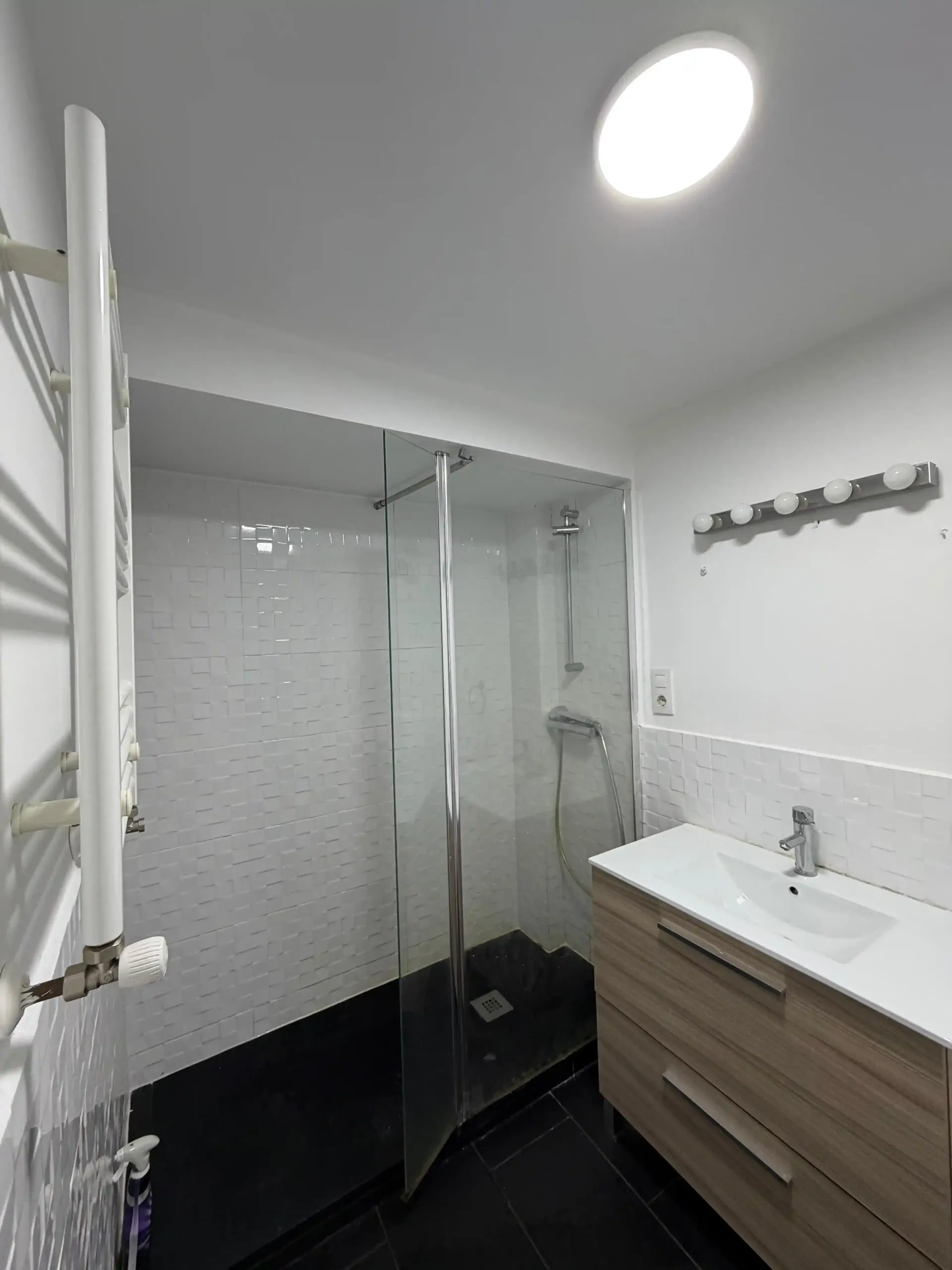 Baño moderno con ducha de cristal, lavabo blanco, paredes grises y plato de ducha con azulejos negros.