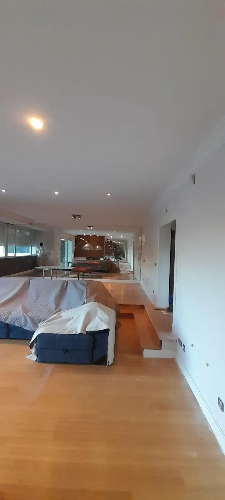 Amplio salón con suelo de madera, paredes blancas y un sofá tapizado en azul que da a una gran zona diáfana.