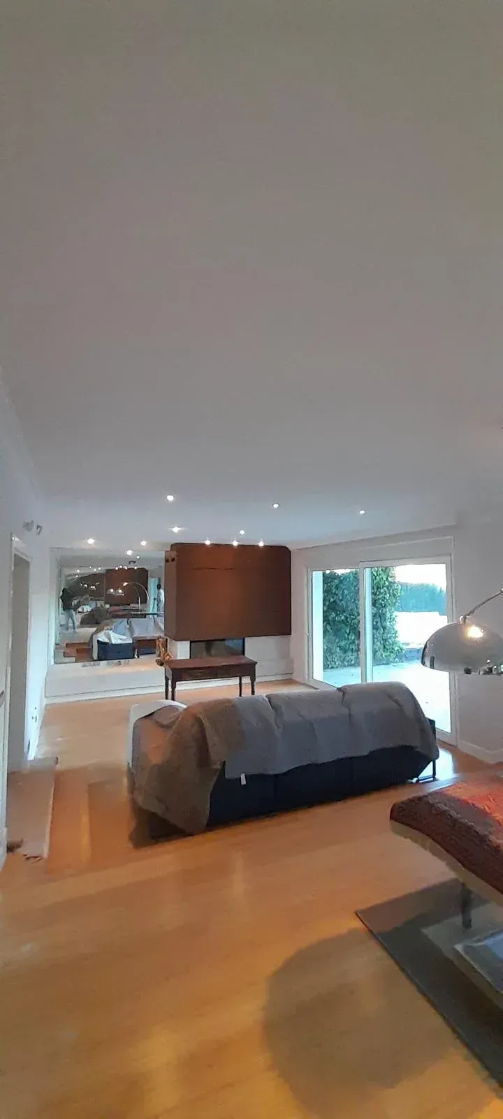 Dormitorio moderno con cama hecha, muebles de madera, espejo grande y vista a la ventana luminosa.
