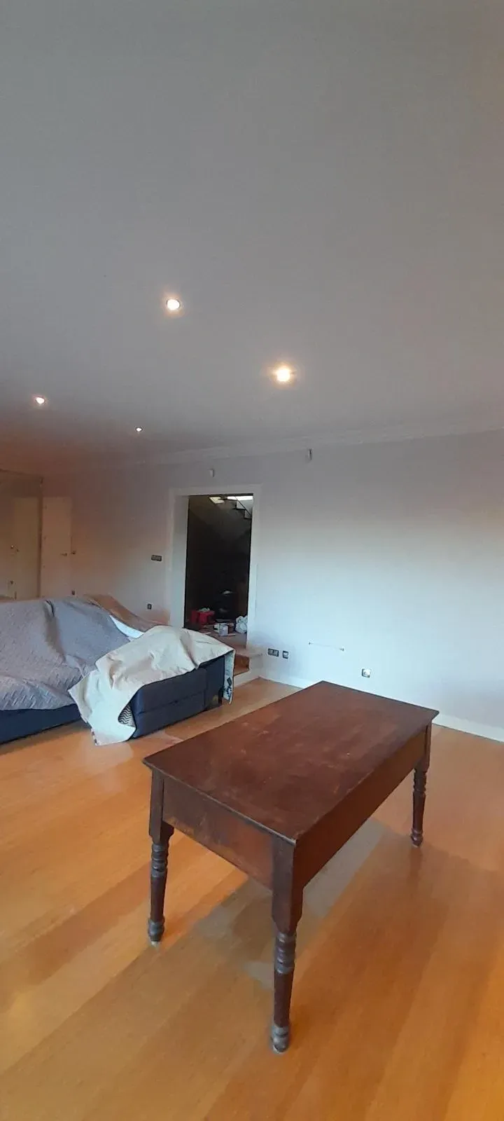 Habitación vacía con una mesa de madera, una cama y luces empotradas en el techo.