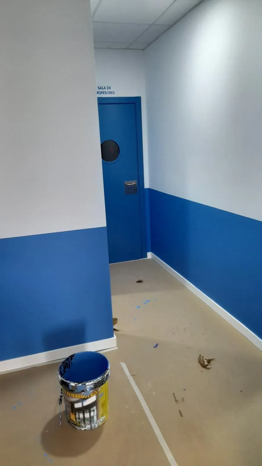 Pasillo en proceso de pintura, con paredes azules y blancas y un cubo de pintura en el suelo.