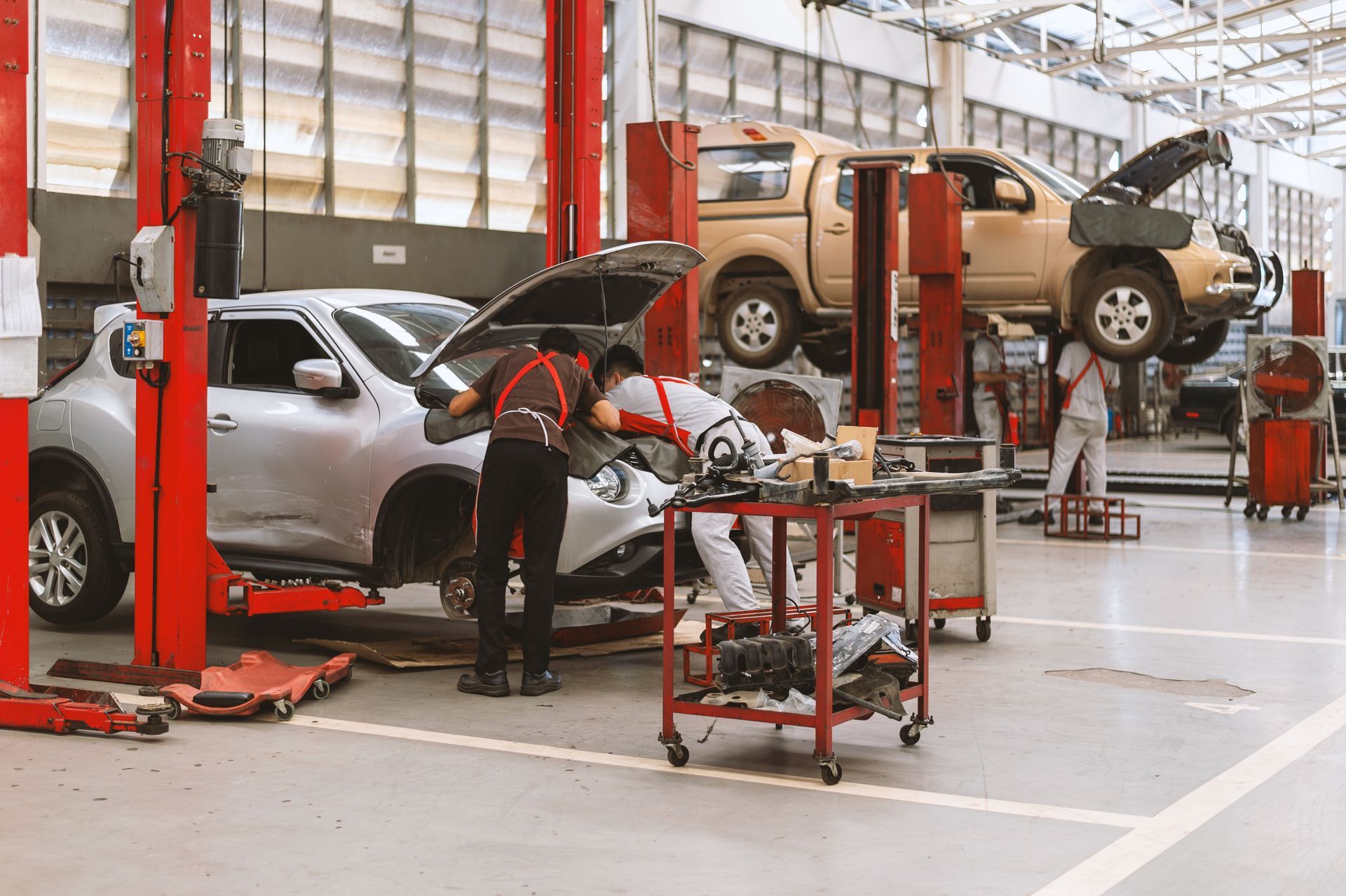 Autowerkstatt mit zwei Fahrzeugen auf Hebebühnen, Mechaniker arbeiten.