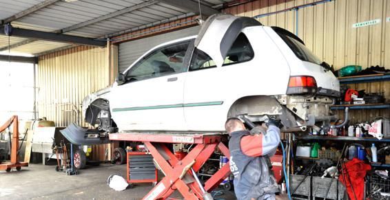 Un mécanicien travaille sur une voiture blanche soulevée par un pont élévateur dans un garage.