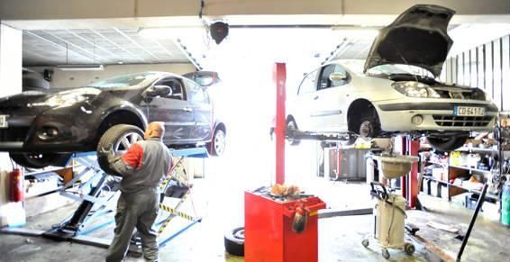 Un mécanicien change un pneu dans un garage ; deux voitures sur des ponts élévateurs, des outils, un intérieur lumineux.