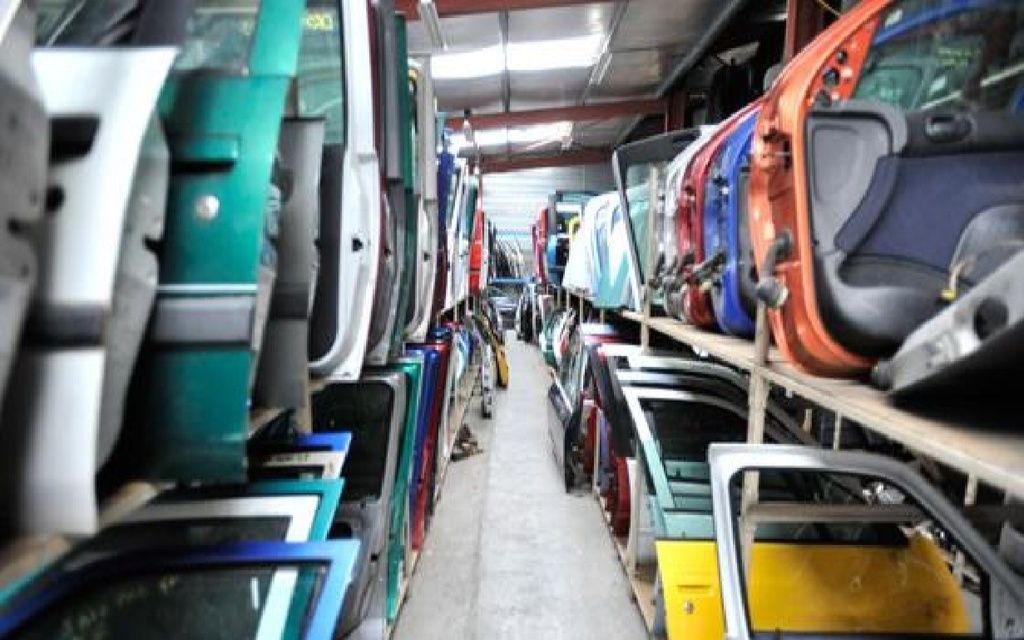 Des rangées de portières de voiture colorées, entreposées sur des étagères dans une casse.