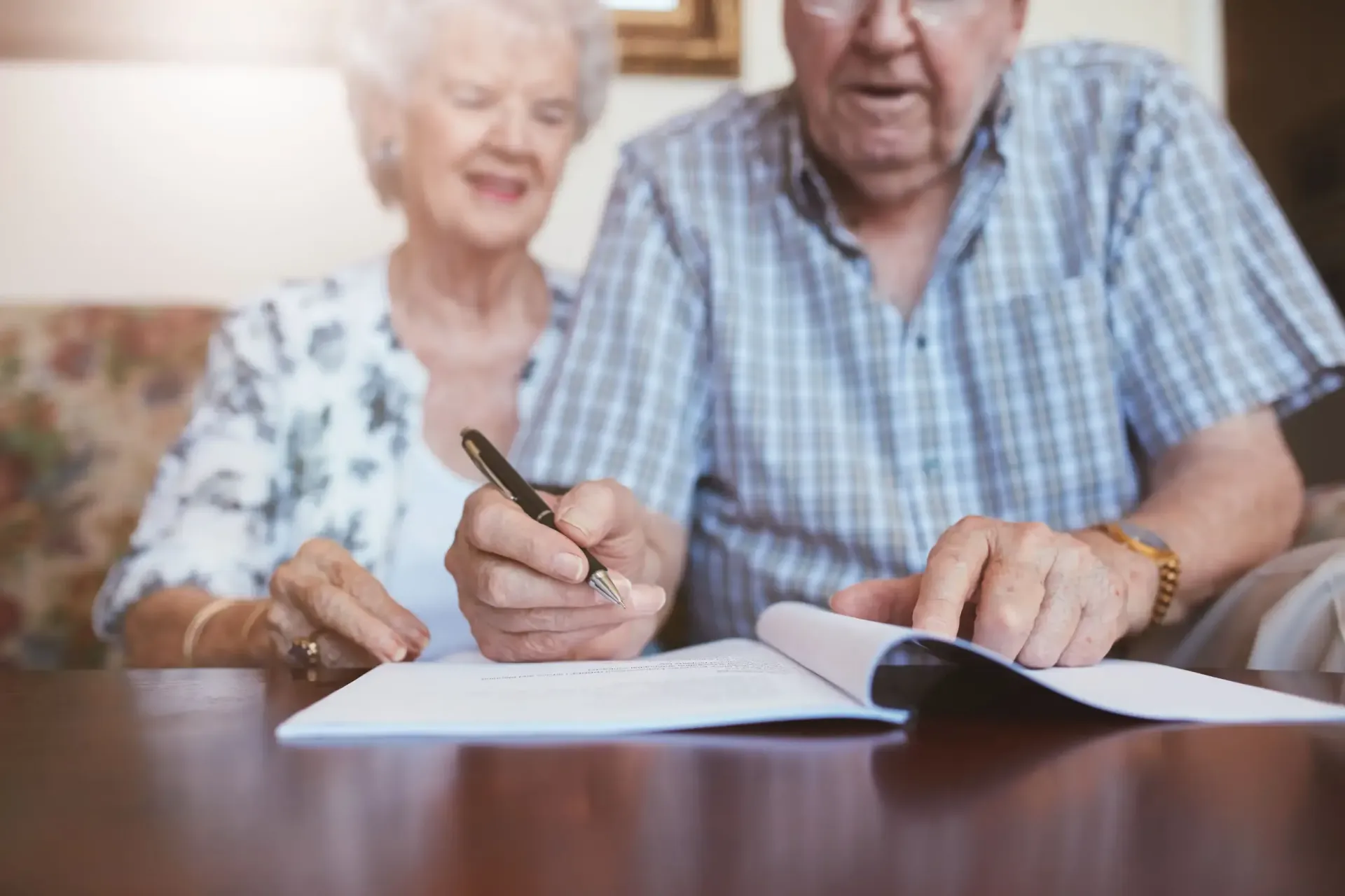 Una pareja de ancianos está sentada en una mesa escribiendo en un trozo de papel.