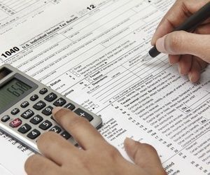 Una persona está llenando un formulario de impuestos con un bolígrafo y una calculadora.