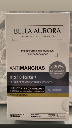 Caja de crema antimanchas Bella Aurora, envase blanco y dorado con detalles morados, sobre una superficie beige.
