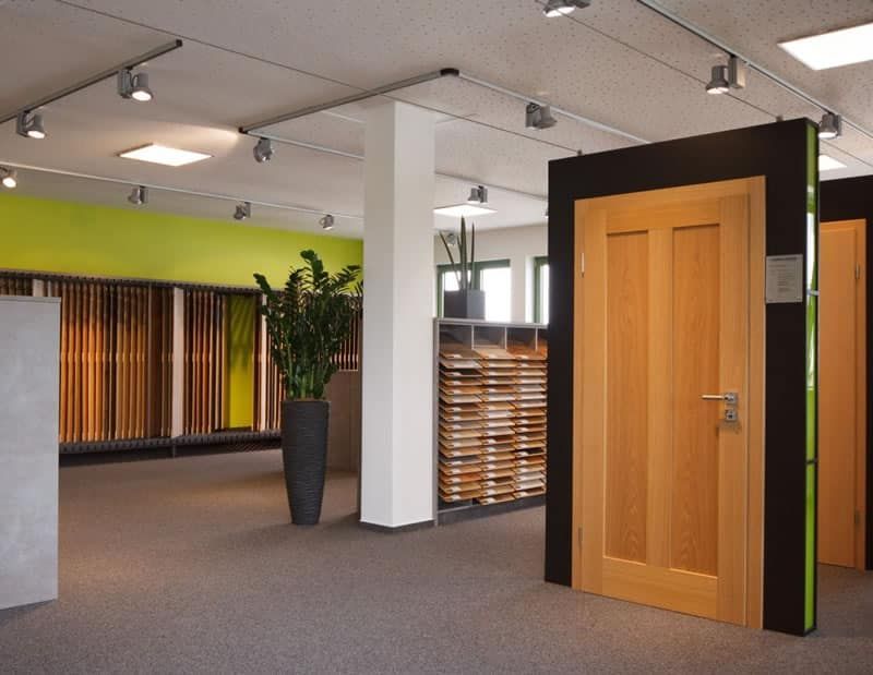 Modernes Bürointerieur mit Holztür, Teppichboden und weißen Säulen unter Deckenleuchten