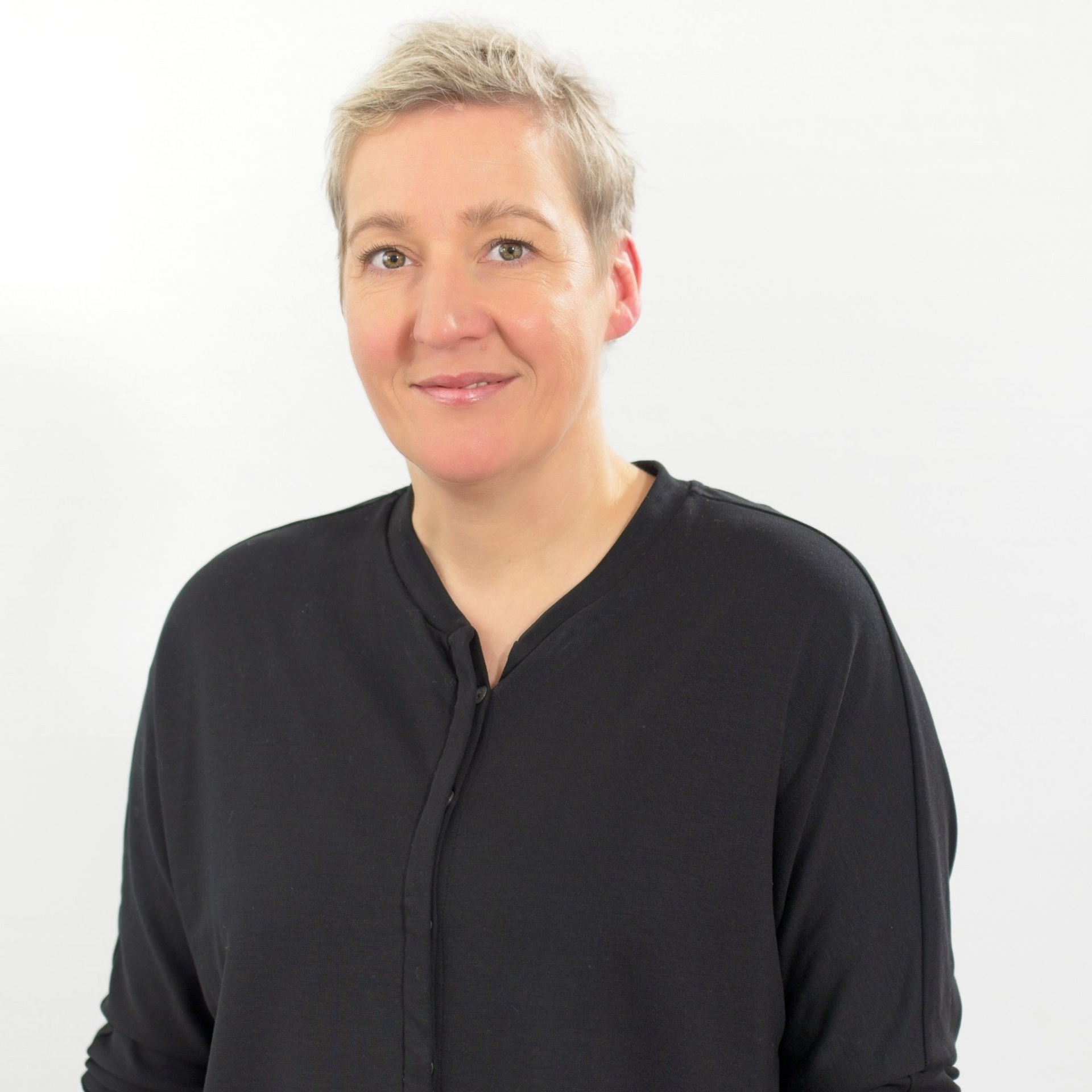 Eine Frau in einem weißen Hemd lehnt an einer weißen Wand.