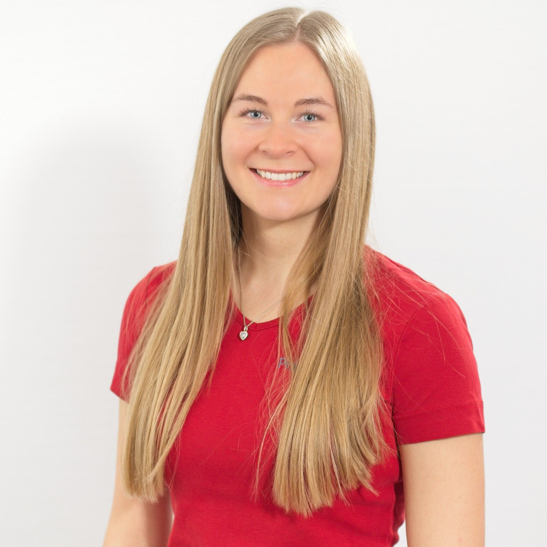Eine Frau in einem roten Poloshirt steht vor einer weißen Wand.