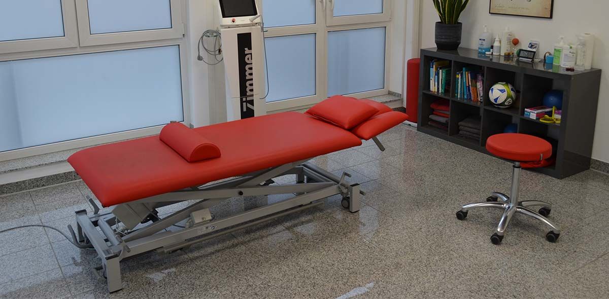 Eine rote Massageliege in einem Raum mit einem Hocker