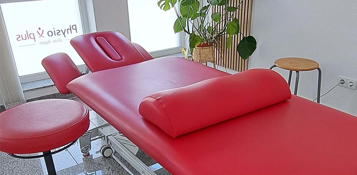 Eine rote Massageliege mit einem Holzhocker in einem Zimmer