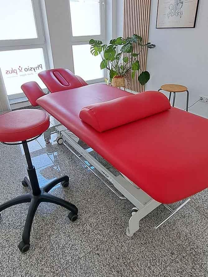 In einem Raum steht neben einem Hocker eine rote Massageliege.