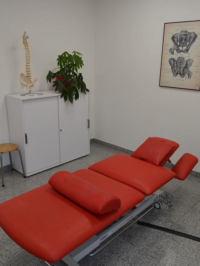 Ein roter Massagetisch in einem Raum mit einem Skelett an der Wand