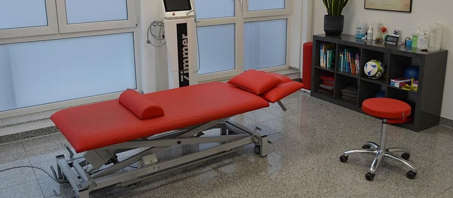 Eine rote Massageliege in einem Raum mit einem Hocker