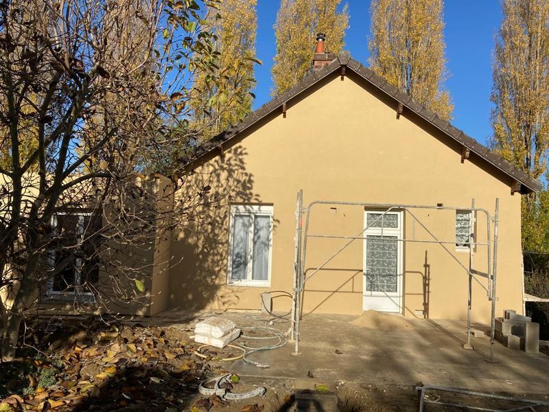 Maison beige en construction, avec échafaudages, fenêtres et toit marron sur fond de ciel bleu.