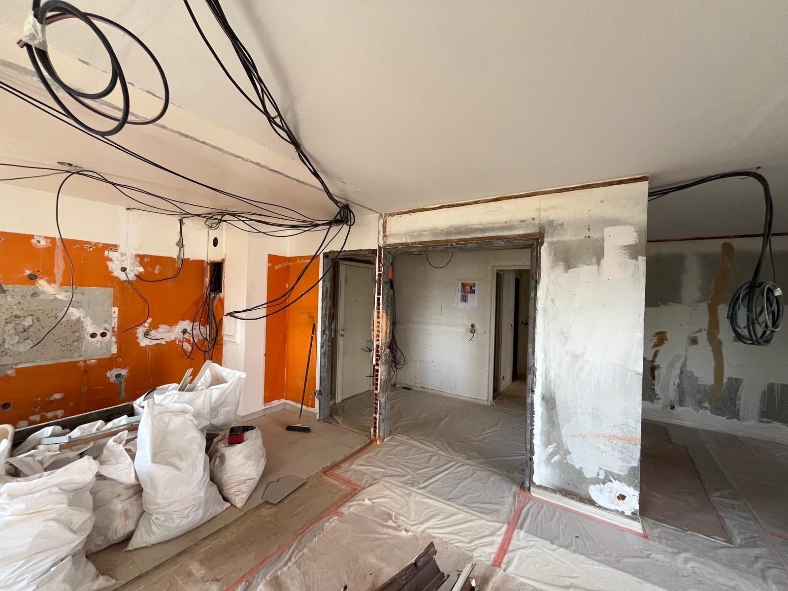 Pièce en rénovation avec des câbles apparents, des sacs de débris et des murs inachevés.